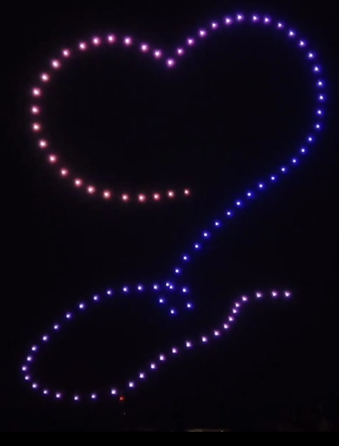 Grand cœur lumineux formé par des drones en vol dans un ciel noir