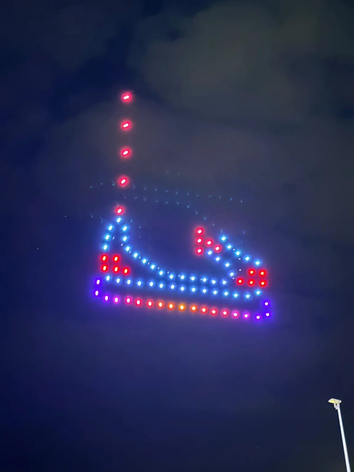 Forme lumineuse aux couleurs bleu, rouge et violet dessinée par des drones dans le ciel